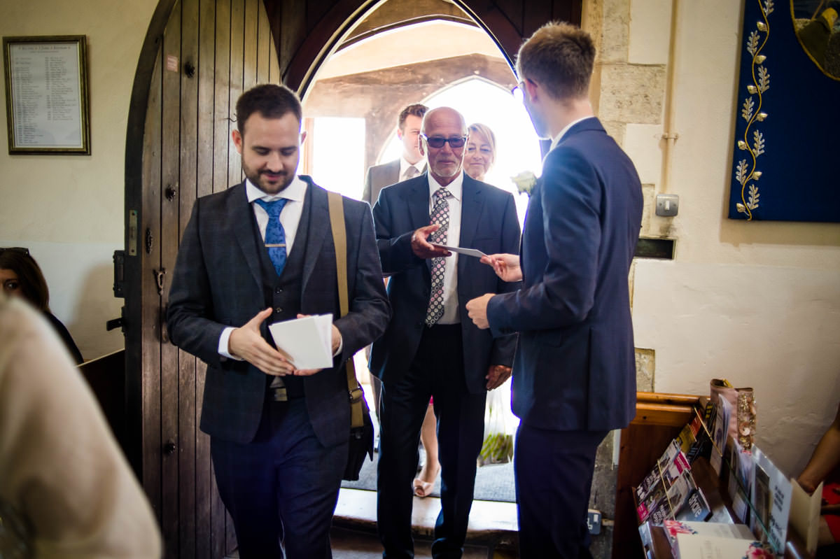 groomsmen handing out orders of service before the wedding in west sussex
