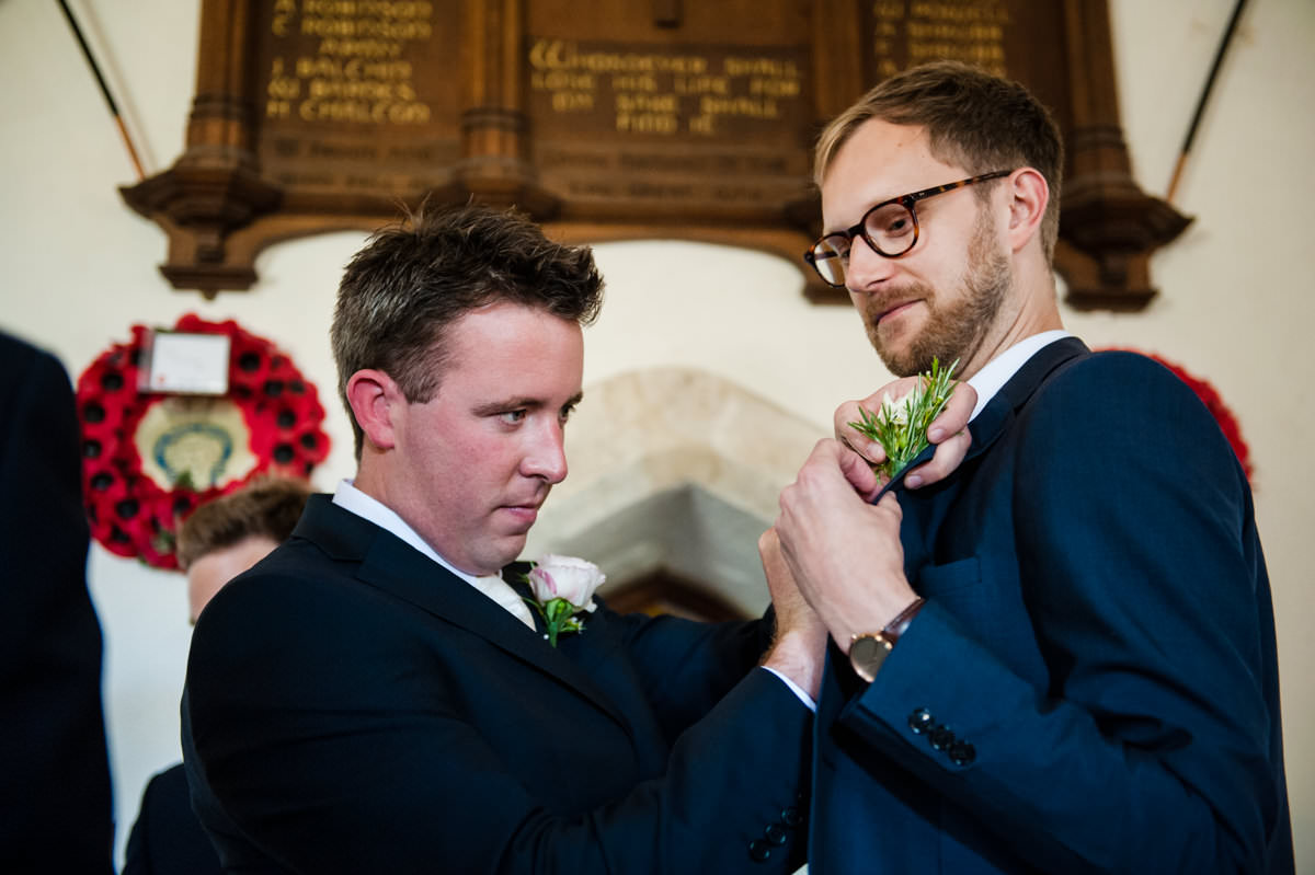 groom helping guest to put on wedding button hole