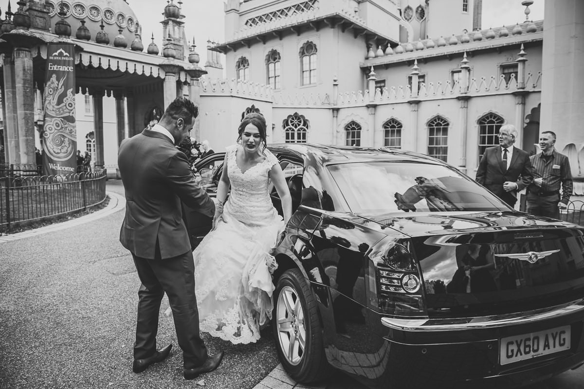Handsome groom helps his beautiful bride out of their wedding car ready for their wedding ceremony at the pavilion
