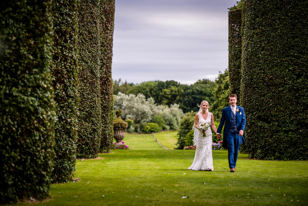 Bride & Groom walking through the stunning hedges in the gardens of Arley Hall