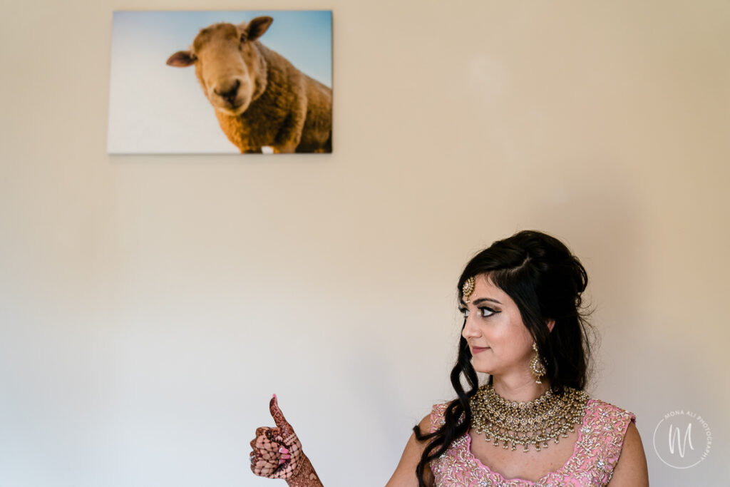 Indian bride giving the thumbs up to her mum whilst overlooked by a photo of a sheep on the wall
