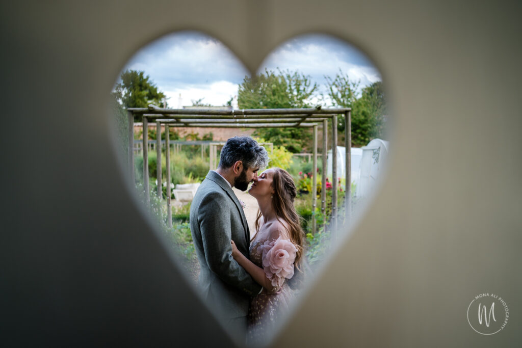 Bride and groom kissing through a heart shape in a door