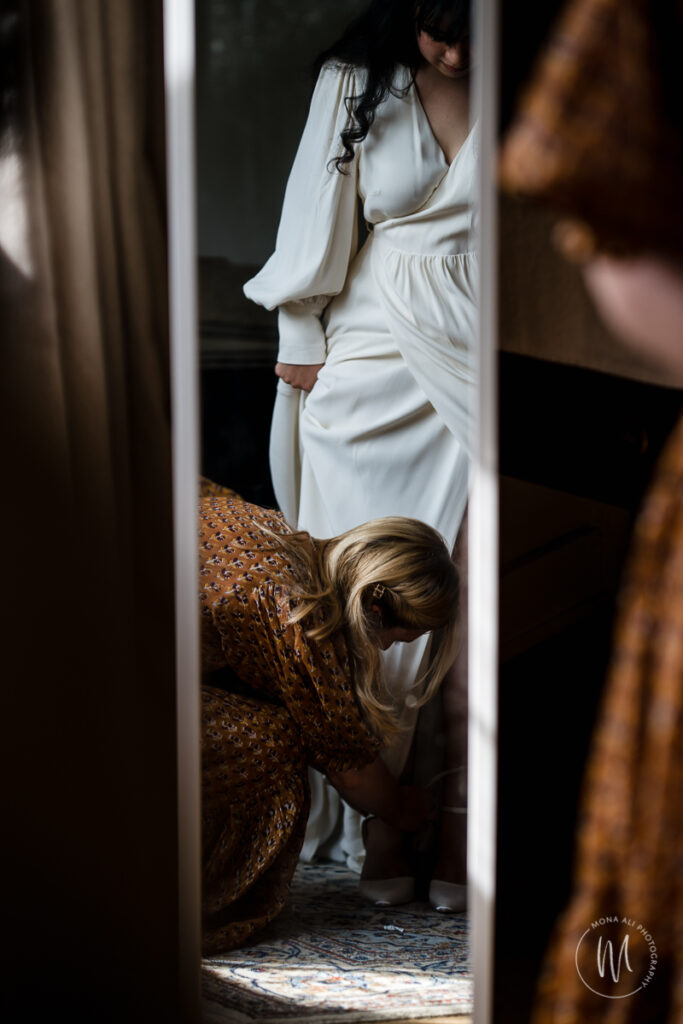 Details of bride's dress as bridesmaid is doing her shoes up